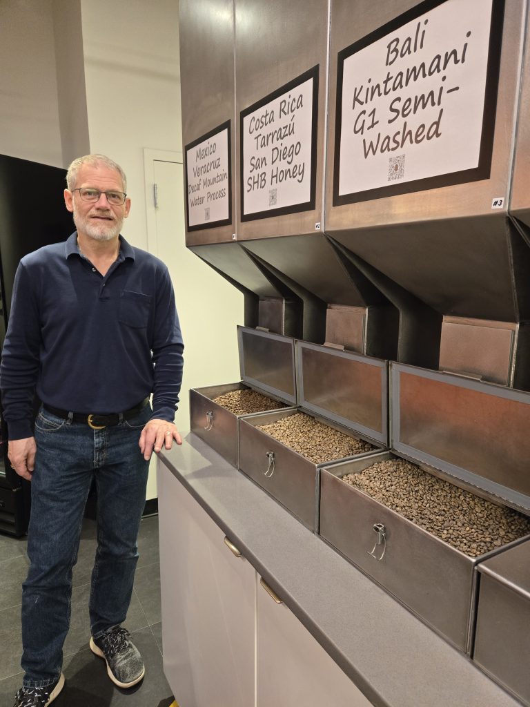 Doug Ilg (Roast Master) standing in front of a selection of 3 green coffee beans